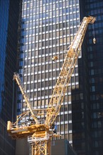 Low angle view of crane against skyscraper