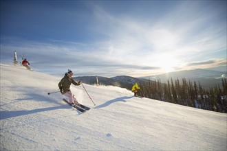 Three people on ski slope at sunlight