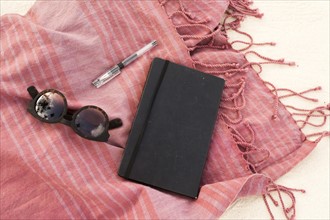 Scarf, notebook, pen and sunglasses on sand