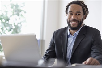 Smiley businessman sitting at desk with laptop.