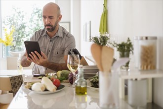 Man using digital tablet leaning on kitchen counter.