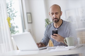 Man working with laptop and holding smart phone at table.