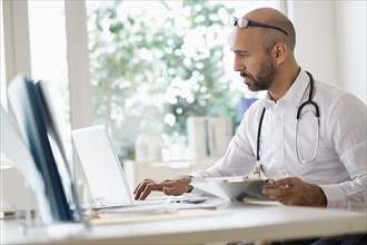Concentrated doctor working with laptop at desk in office.