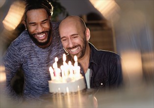 Smiley homosexual couple looking at birthday cake.