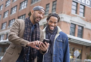 Smiley homosexual couple looking at smart phone in street.