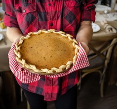 Woman holding baked pumpkin pie for Thanksgiving.