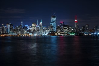 Illuminated cityscape reflecting in river. New York City, New York, USA.