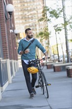 Man walking with bicycle in city.