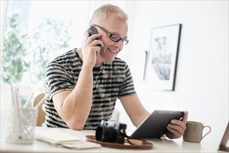 Man in home office using smartphone and tablet.
