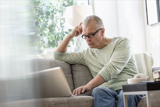 Man sitting on sofa using laptop at home.