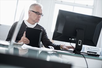 Man working in office using computer and tablet.