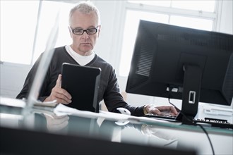 Man working in office using computer and tablet.