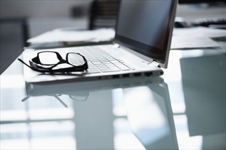 Eyeglasses and laptop on desk in office.