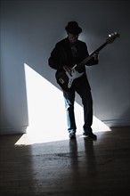 Man playing bass guitar in empty room.