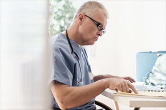 Man in scrubs using laptop in doctor's office.