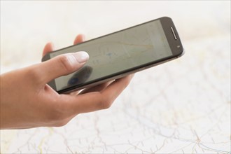 Hand holding smart phone, map in background.
