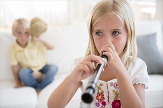 Girl (6-7) playing flute and boy (4-5) sitting on sofa