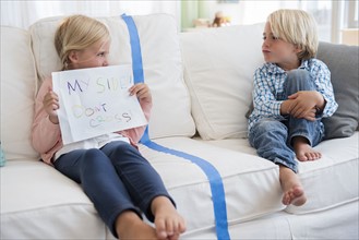 Boy (4-5) sitting on sofa with girl (6-7) holding paper
