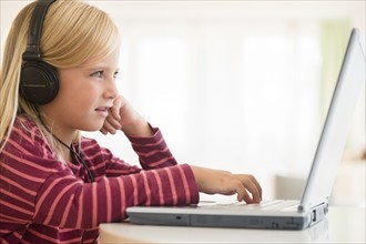 Girl (6-7) wearing earphones, using laptop