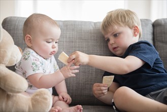 Brother (2-3) sharing crackers with baby sister (12-17 months)