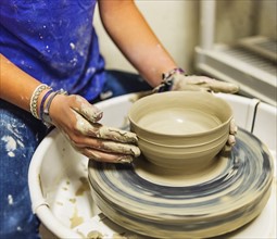 Woman shaping clay bowl on pottery wheel