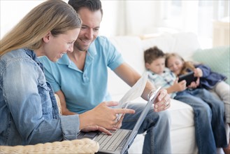 Man and woman paying bills with two children (6-7, 8-9) sitting on sofa, using digital tablet