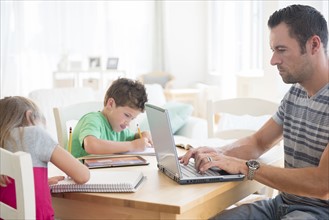 Man using laptop with two children (6-7, 8-9) writing in notepads