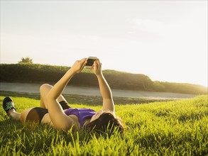Young woman lying on grass using phone