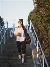 Young woman with smoothie walking down stairs