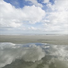 Reflection of clouds in puddle, sea in background