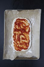 Pizza dough with tomato sauce on wax paper