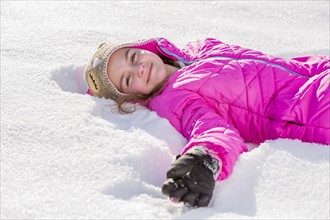 Girl (10-11) in pink jacket lying in snow