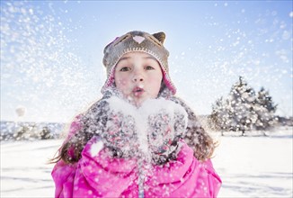 Girl (10-11) in pink jacket blowing snow