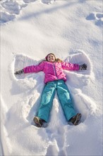 Girl (10-11) in pink jacket making snow angel