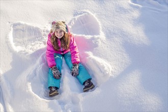 Girl (10-11) in pink jacket sitting in snow