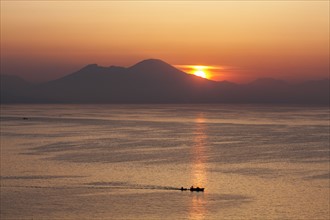 Silhouette of boat on sea with mountains in background at sunset
