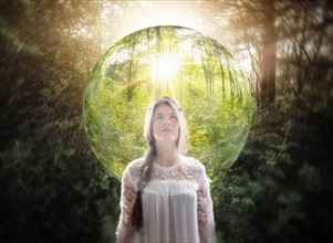 Young woman in forest looking at transparent sphere.