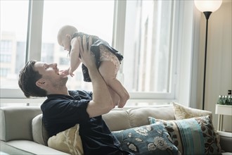 Father sitting on sofa and playing with baby daughter (2-5 months).