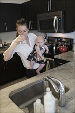 Mother drinking water while holding baby daughter (2-5 months).