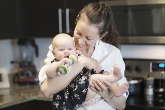Mother playing with baby daughter (2-5 months) in kitchen.