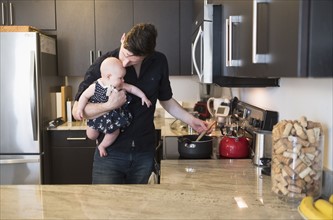 Father kissing baby daughter (2-5 months) while stirring food.