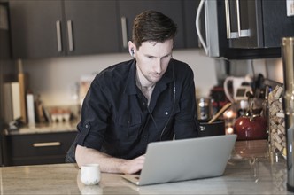 Man working on laptop computer in kitchen.