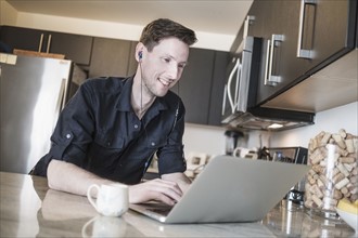 Man smiling while working on laptop computer in kitchen.