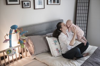 Mother kissing baby daughter (2-5 months) in bedroom.