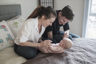 Parents playing with baby daughter (2-5 months) in bedroom.
