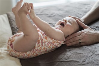Father playing with daughter (2-5 months) on bed.
