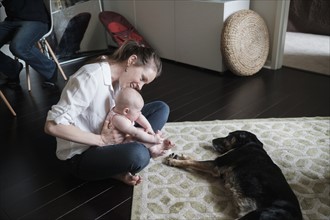 Mother holding baby (2-5 months) and playing with dog.