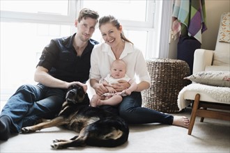 Portrait of happy family sitting on carpet with daughter (2-5 months) and dog.