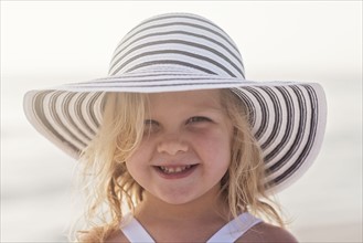 Portrait of girl (4-5) in sunhat at beach