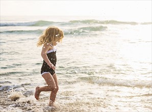 Girl (4-5) running in water on beach